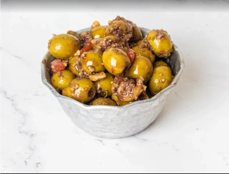 Bowl of Zeytoon Parvardeh, Persian marinated olives with walnuts and pomegranate arils, on a wooden board