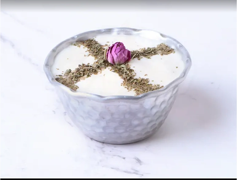 A bowl of thick white Persian shallot yogurt dip topped with dried rose petals and mint.