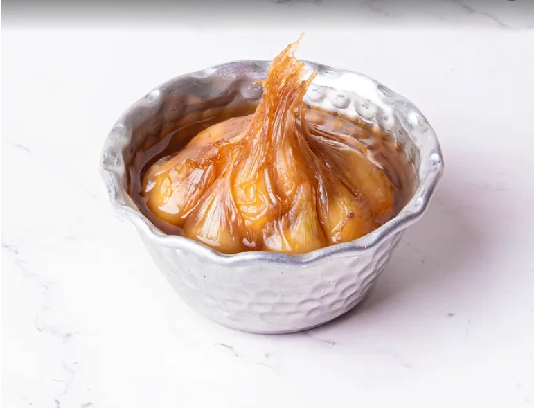 Jar of dark Torshi Seer Persian pickled garlic on a wooden table